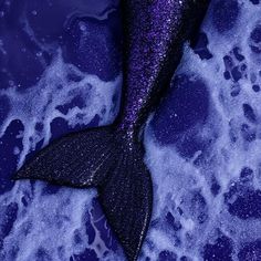 a purple and black mermaid tail laying on top of the ocean water with bubbles around it
