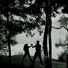two people standing on a dock in the woods holding each other's hands and punching their fists
