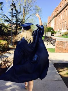 a woman in a graduation gown is walking down the sidewalk with her arms raised up