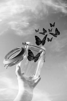 a hand holding a glass jar with butterflies flying out of it in the blue sky
