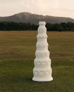 a tall white wedding cake sitting on top of a lush green field with mountains in the background