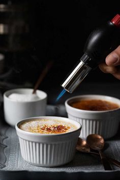 a person is pouring something into small white bowls with spoons next to them on a tray