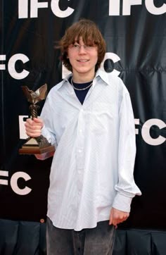 a young boy holding an award in front of a black backdrop with white letters on it
