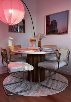 a round table with chairs around it and a pink lamp hanging from the ceiling above