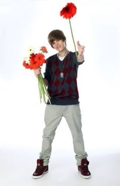 a young man holding flowers and giving the peace sign with his hand while standing in front of a white background