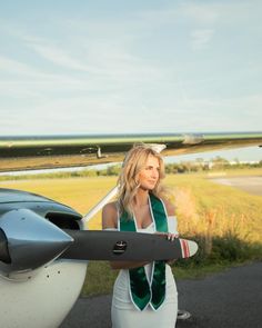 a woman standing next to an airplane with her hand on the wing and looking off into the distance
