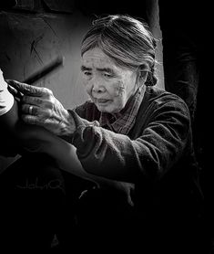 an old woman is working on something in the dark with one hand and another arm