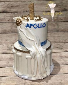a white cake with gold decorations and an aculo logo on the top is sitting on a wooden table