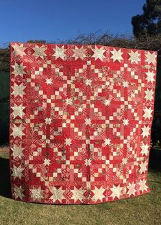 a red and white quilt hanging from a clothes line in the grass with trees in the background