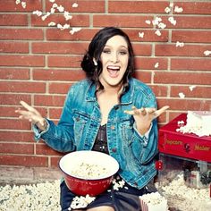 a woman sitting in front of a brick wall with popcorn all over her body and hands