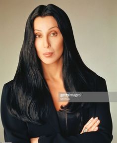a woman with long black hair posing for the camera, wearing a black suit and diamond ring