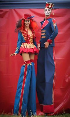a man and woman in costume standing next to each other near a red wall with a large banner behind them
