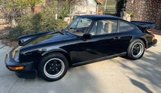 a black porsche sits parked in front of a house