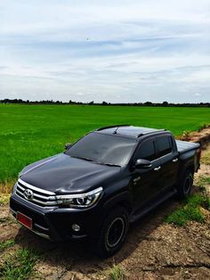 a black truck parked on the side of a dirt road in front of a green field