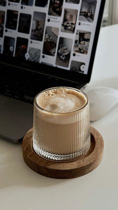 a cup of coffee sitting on top of a wooden coaster next to a laptop computer