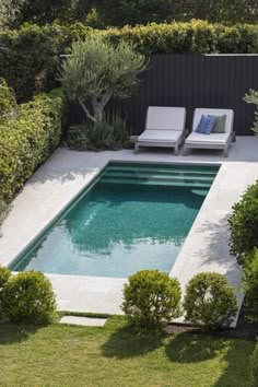 an empty swimming pool surrounded by shrubbery and lawn furniture with two lounge chairs next to it