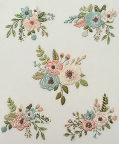 four embroidered flowers on white fabric with green leaves and pink, blue, and yellow flowers