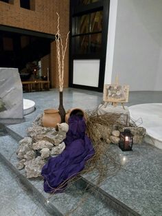 there is a purple cloth on the ground next to some rocks and a vase with a tree in it