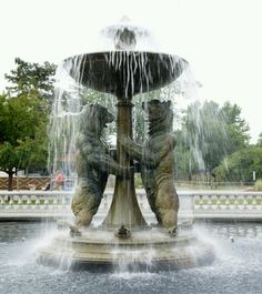 two bears sitting on top of a fountain with water shooting from it's sides