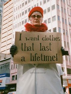 a man holding a sign that says i want clothes that last a life time in front of tall buildings