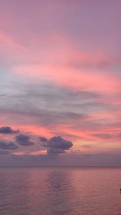 a boat sitting on top of a large body of water under a pink and blue sky