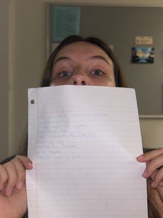 a woman holding up a piece of paper with writing on it in front of her face