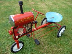 an old red tractor with a blue disc attached to it's front wheel, sitting in the grass