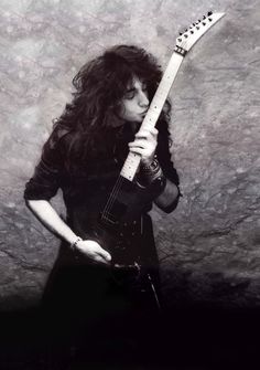 a man with long hair holding an electric guitar in his right hand and posing for the camera