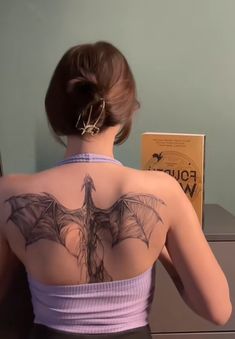 a woman with a bat tattoo on her back sitting in front of a bookshelf
