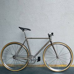 a silver and gold bike parked against a wall with no one on the front wheel