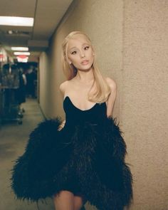a woman standing next to a wall wearing a black dress and ostrich feathers
