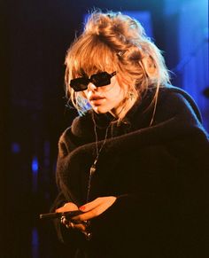 a woman wearing sunglasses and holding a cell phone in her right hand while looking at the screen