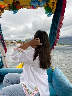 a woman sitting on top of a blue boat in the middle of the ocean holding her hand up to her face
