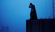 a batman statue on top of a building with the city skyline in the back ground