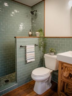 a white toilet sitting in a bathroom next to a wooden cabinet and shower stall with green tiles on the walls