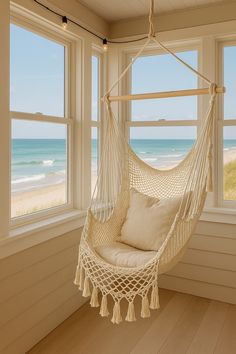 a white hammock hanging from a window next to a beach and the ocean