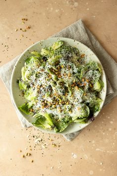 a white plate topped with broccoli covered in cheese and seasoning next to a napkin