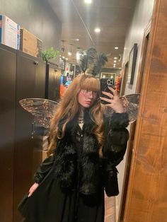 a woman taking a selfie in front of a mirror wearing a black dress with feathers on it