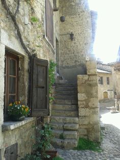 an old stone building with stairs leading up to the door and flowers growing on the window sill