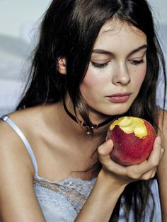 a woman is holding an apple in her right hand and looking down at the fruit