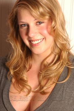 a beautiful blonde woman with blue eyes and long hair smiling at the camera while wearing a gray shirt