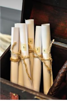 four white candles are tied together in a wooden box with brown leather handles and rope