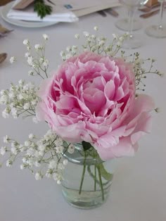 a vase filled with pink flowers sitting on top of a white table covered in place settings