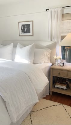 a bed with white linens and pillows in a bedroom next to a lamp on a table