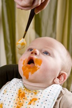 a baby is being fed with orange sauce on his face by an adult holding a spoon