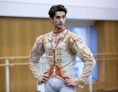 a man dressed in white and gold is standing with his hands on his hips as if he's about to dance