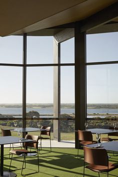 an empty restaurant with large windows overlooking the ocean and grass on the floor is very nice