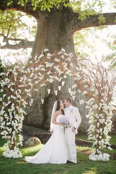 a bride and groom are standing under an arch with flowers on the branches in front of them