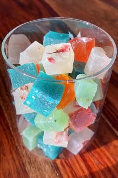 a glass filled with colorful gummy bears on top of a wooden table