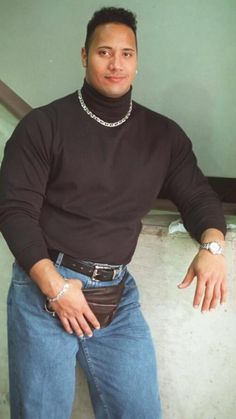 a man in jeans and a turtle neck sweater poses for a photo with his hands on his hips